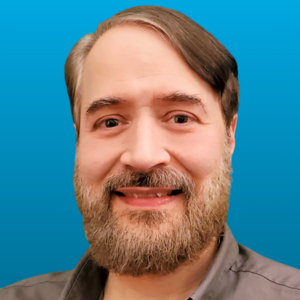 Portrait of Carl Burkart against a blue background, featuring a smiling man with a beard, showcasing professionalism and approachability.