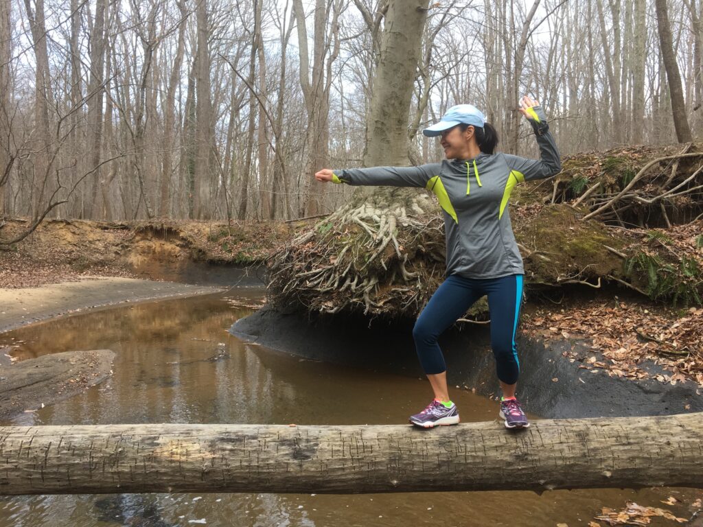 Liani hiking, balancing on a log over a stream in the woods. New MMI Direct team member enjoying outdoor activities.